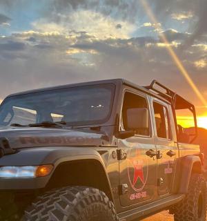 a jeep in the desert with the sunset in the background