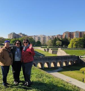 three people standing in the grass near a bridge