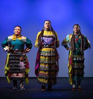 three women in traditional costumes on a stage