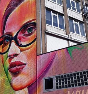 ein großes Wandbild einer Frau mit Brille an einem Gebäude