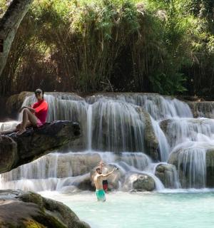 two people sitting on a tree branch in a waterfall