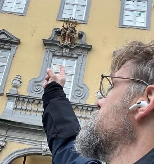 Ein Mann steht mit erhobener Hand vor einem Gebäude