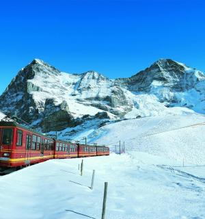 一列红色火车在白雪皑皑的山峰附近的铁轨上行驶