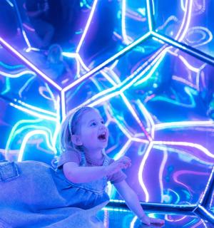 a little girl sitting in a room with neon lights