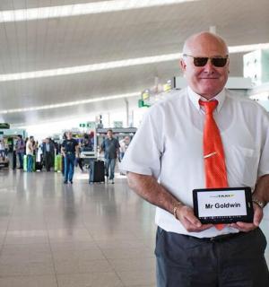 一名男子在机场打着红领带，举着牌子