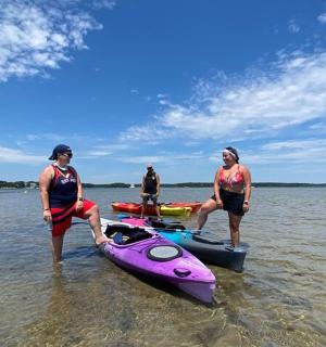 tři lidé stojící ve vodě vedle růžového kajaku