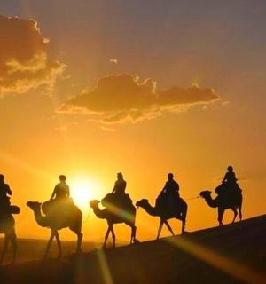 un grup de persones muntant a cavall al desert a la posta de sol