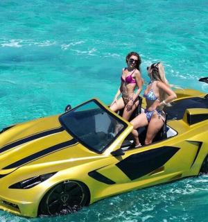 two girls are sitting on a yellow super car in the water