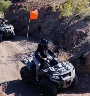 two people riding on atvs on a dirt road