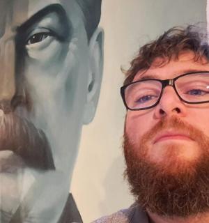 a man with glasses standing in front of a painting