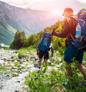 dva lidé s batohy jdoucí po horském potoku