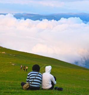 dva lidé sedící na travnatém kopci a dívající se na mraky