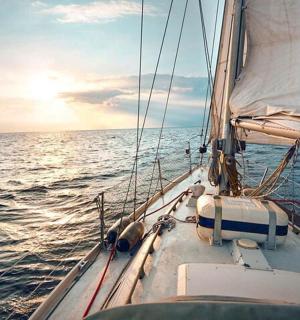 a sail boat in the ocean with the sun setting