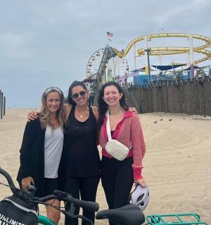 three women standing on the beach with a roller coaster