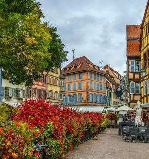 miesto gatvė su pastatais, kėdėmis ir gėlėmis