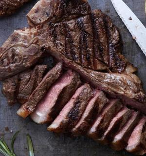 a table with a steak and a knife and a cutting board