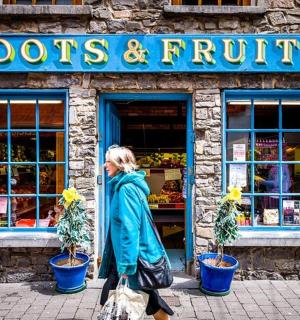 žena kráčející před obchodem s kořeny a ovocem