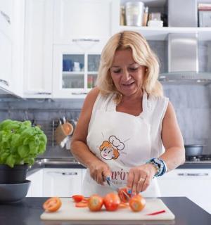 una dona a la cuina tallant tomàquets en una taula de tallar