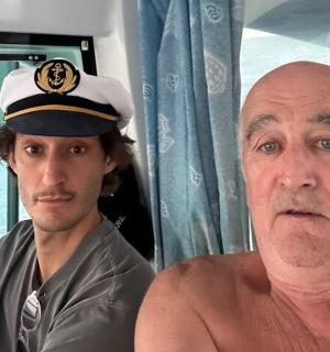 a shirtless man sitting next to a man wearing a sailor hat