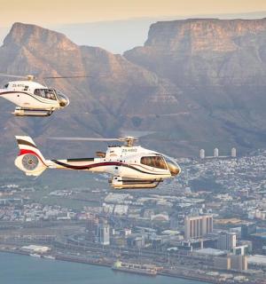 two helicopters flying over a city with a mountain in the background