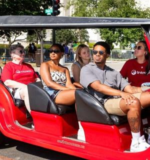 skupina lidí jedoucích v červeném golfovém vozíku