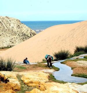 two people standing in the sand next to a stream