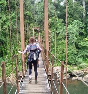 a woman crossing a suspension bridge over a river