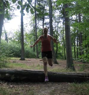 a man running across a fallen log in the woods