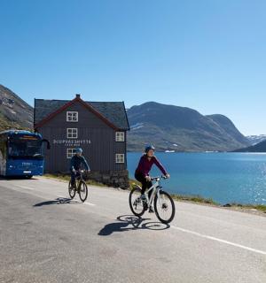 two people riding bikes on a road next to a lake