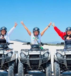 Skupina tří lidí jedoucích na čtyřkolkách na pláži