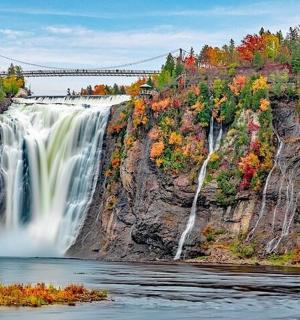 a waterfall on a cliff with a bridge in the background