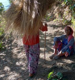 two women sitting on the ground under a pile of grass