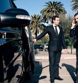 两名西装革履的男子在车旁行走，用手机通话