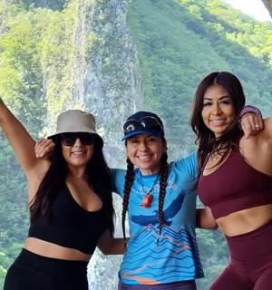 three women are standing in front of a waterfall