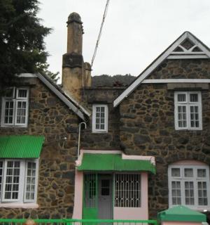 一座有着白色窗户和绿色百叶窗的古老石屋