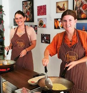 two women in a kitchen preparing food in a wok