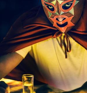 мужчина в маске сидит за столом со стаканом