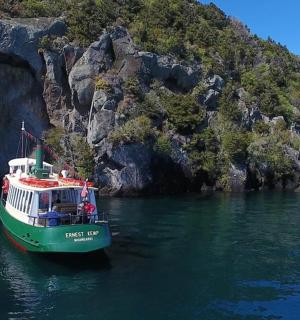 a green and white boat in the water next to a mountain
