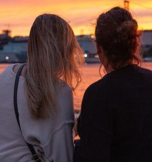 two women standing next to the water at sunset