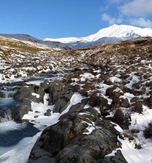 a snow covered mountain with a river and snow covered rocks