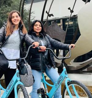two women riding bikes in front of a building