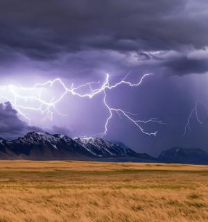 a lightning storm over a field with mountains in the background