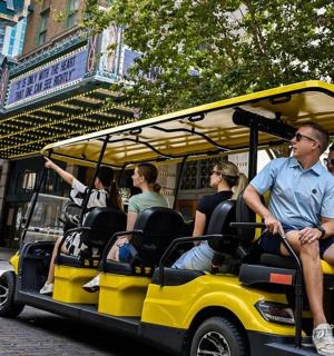 skupina lidí jedoucích po ulici na golfovém vozíku