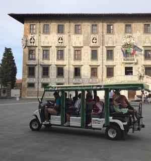 skupina lidí jedoucích na golfovém vozíku před budovou