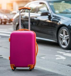 一辆粉色的行李箱停在路边的一辆汽车旁