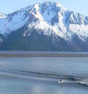 a person riding a wave in the water with snow covered mountains