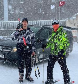 deux personnes à skis dans la neige devant une voiture