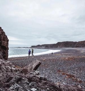 two people walking on a rocky beach near the ocean