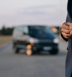 一名身着西装的男子，背景是一辆汽车