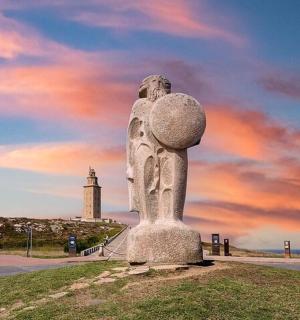 uma estátua na praia com um farol ao fundo